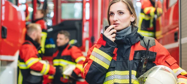 Красива жінка пожежниця з шоломом, що стоїть у пожежній частині — стокове фото