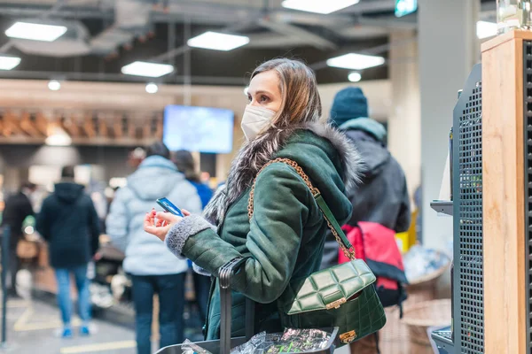 Kadın süpermarkette maske takmış, kasada kuyrukta bekliyor.