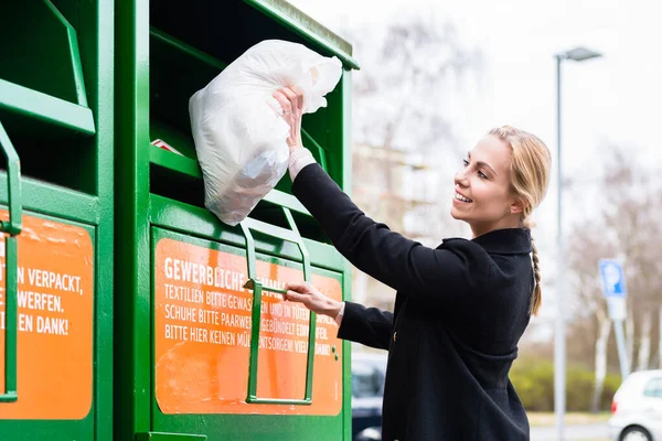 Frau legt alte oder gebrauchte Kleidung in Spendentonne — Stockfoto