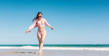 Kumlu bir sahilde, suda yürüyen bir kadın.