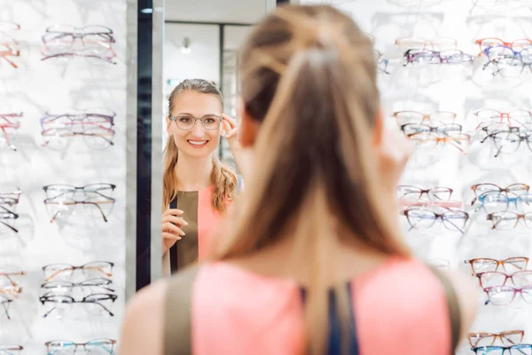 Mujer joven probando gafas de moda en la tienda optometrista —  Fotos de Stock