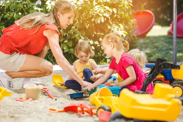 砂の箱で楽しい時間を過ごす子供たちと遊びの学校の先生 — ストック写真