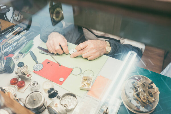 Top-down view on hands of watchmaker sitting at his workbench