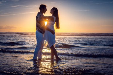 Gün batımında sahilde öpüşen romantik bir çift.