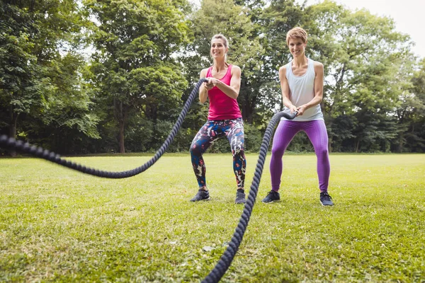 Sonrientes mujeres jóvenes haciendo ejercicio de cuerda de batalla en el parque — Foto de Stock