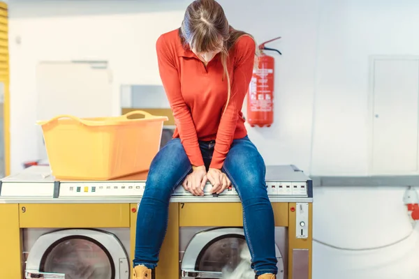 Mulher senta-se na máquina de lavar roupa na lavanderia — Fotografia de Stock