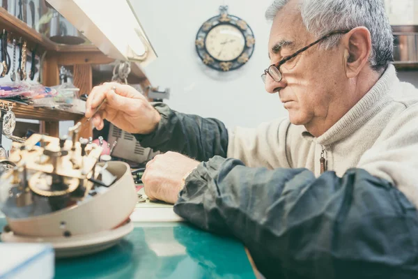 Watchmaker in his workshop repairing a larger clock — Stock Photo, Image