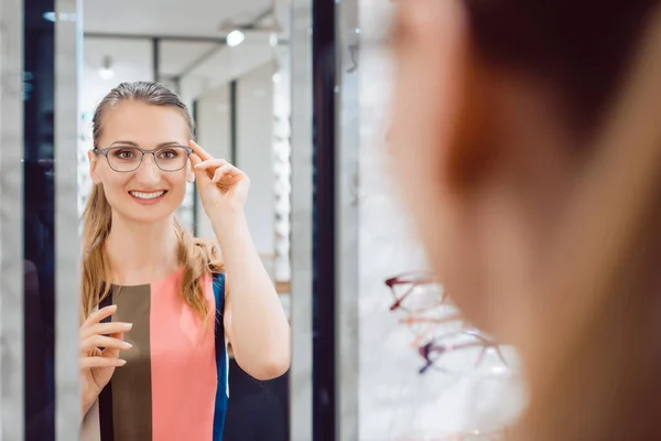 Giovane donna che prova occhiali alla moda nel negozio di optometrista — Foto Stock