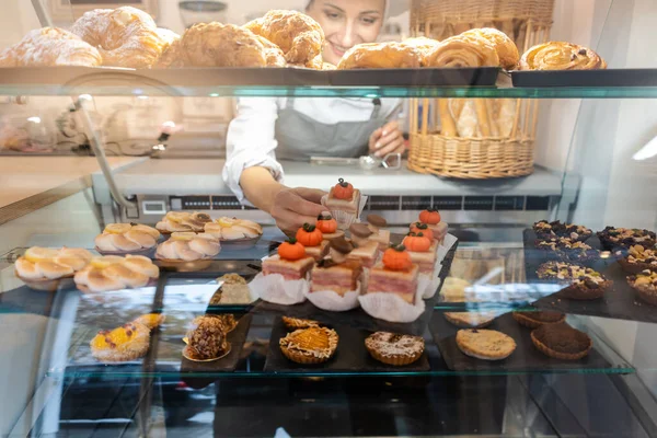 Confectioner shot through glass display in her shop — Stock Photo, Image