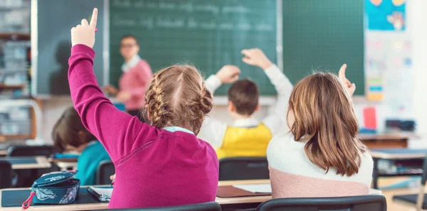 Дві дівчини студенти піднімають руки, щоб відповісти на питання в шкільному класі — стокове фото
