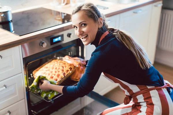 Happy woman removing pie from oven — Stock Photo, Image