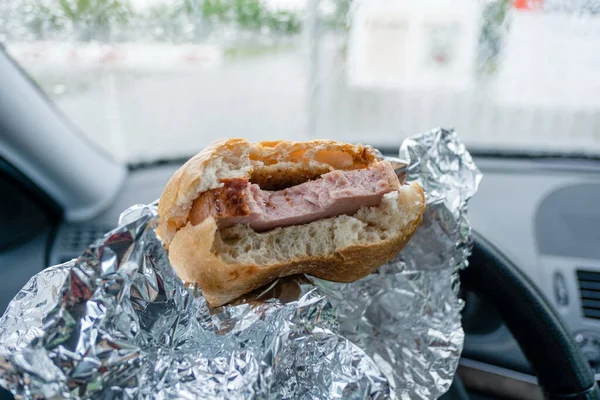 Un homme mange un sandwich à la viande dans une voiture qui attend devant la porte — Photo