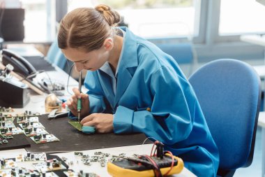 Worker in electronics manufacturing soldering a component clipart