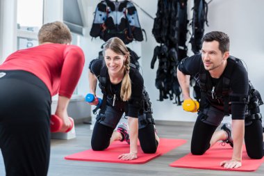 Antrenörlü bir kadın ve erkek, spor salonunda triseps egzersizi yapıyor.