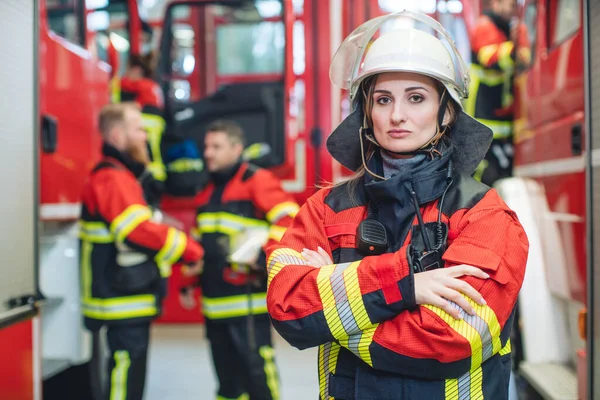 Beautiful fire fighter woman with her helmet standing in the firehouse — Stock Photo, Image