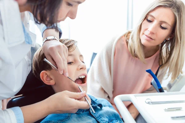 Hasta anne, dişçiden dişlerini muayene eden oğluna bakıyor. — Stok fotoğraf