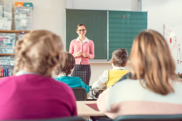 Nauczyciel w klasie szkolnej z uczniami siedzącymi i słuchającymi — Zdjęcie stockowe