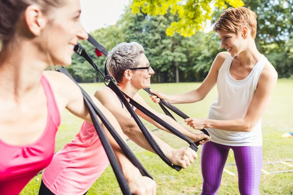 Happy mature athletic woman doing exercises with the female personal fitness trainer in the park — Fotografia de Stock