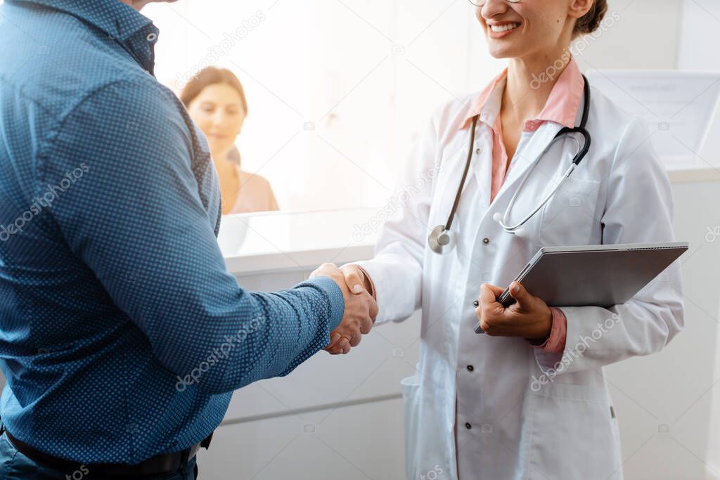 Doctor and patient shaking hands at front desk of doctors office