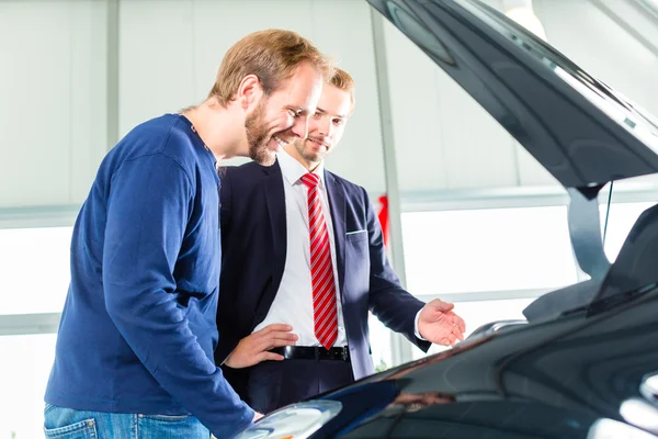 Young man and seller  in car dealership — Stock Photo, Image