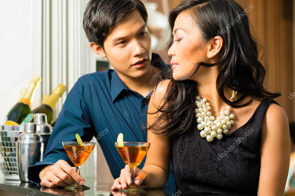 Asian man and woman at bar with cocktails