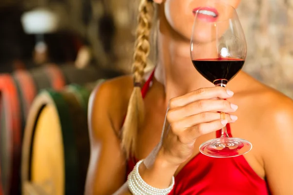 Woman looking at red wine glass in cellar — Stock Photo, Image