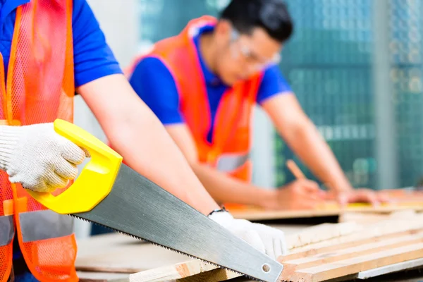 Constructor aserrando una tabla de madera del edificio — Foto de Stock