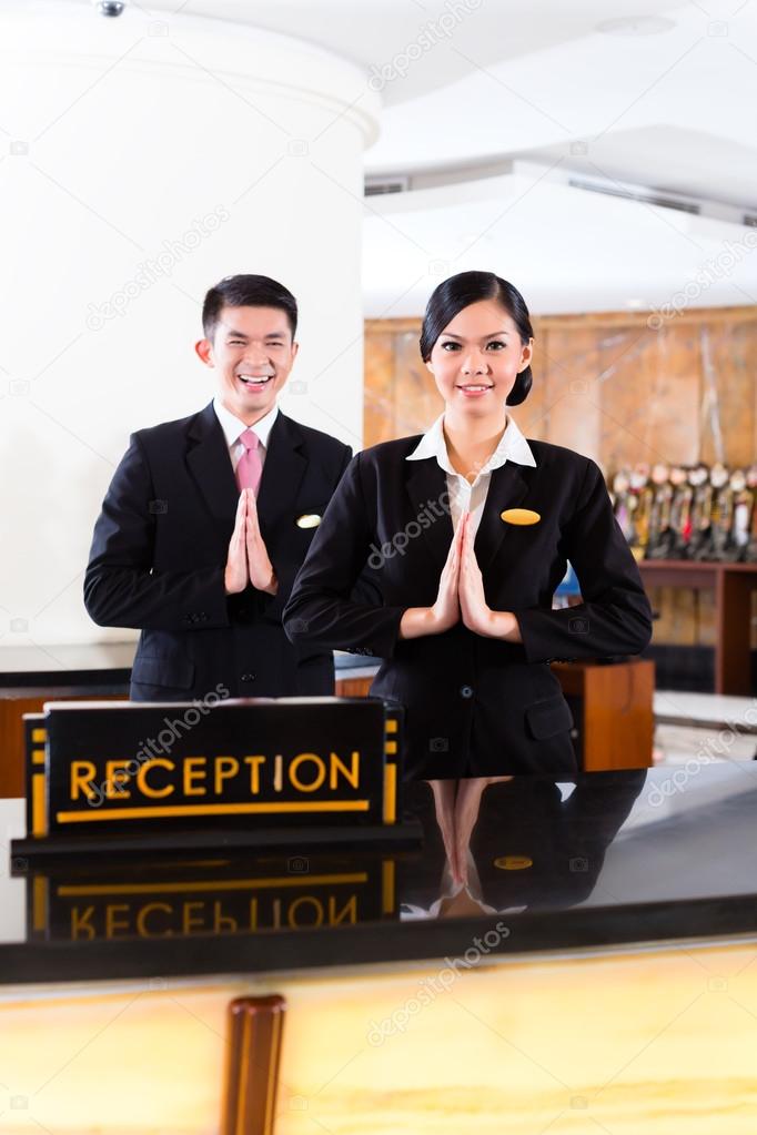 Chinese Asian reception team at luxury hotel front desk welcoming guests with typical gesture, a sign of good service and hospitality