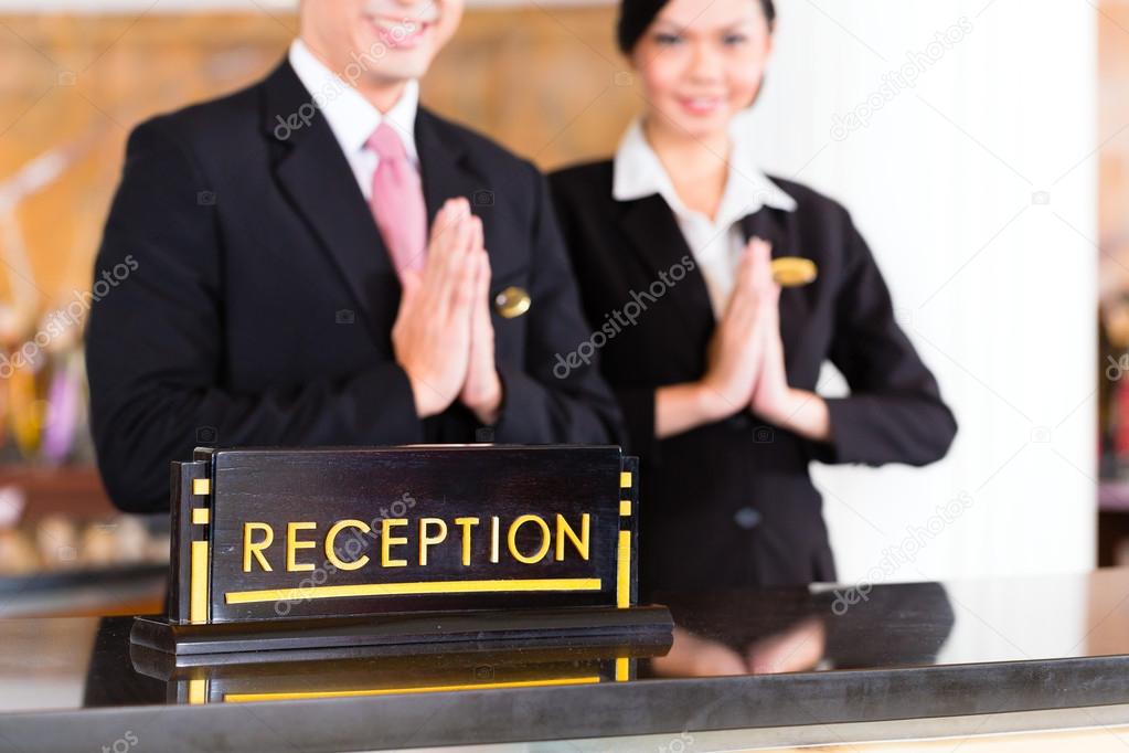 Chinese Asian reception team at luxury hotel front desk welcoming guests with typical gesture, a sign of good service and hospitality