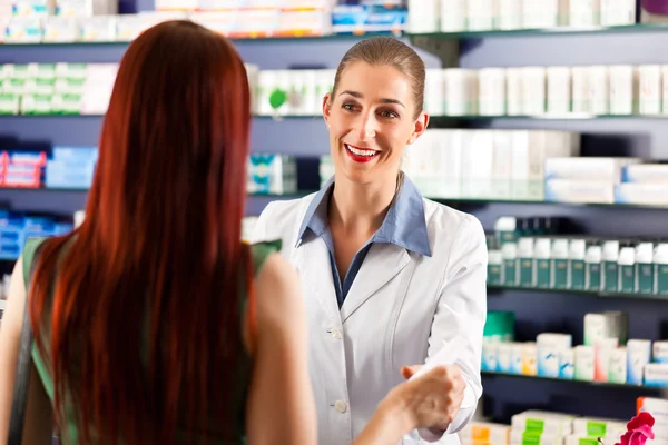 Farmacêutica feminina na farmácia com um cliente — Fotografia de Stock