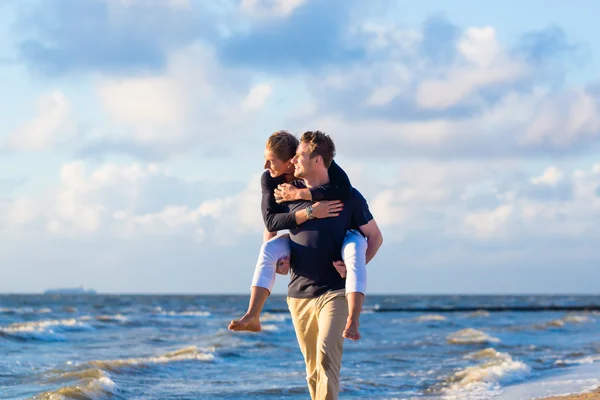 Homem carregando mulher piggyback na praia — Fotografia de Stock