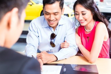 Couple signing sales contract for car at dealership