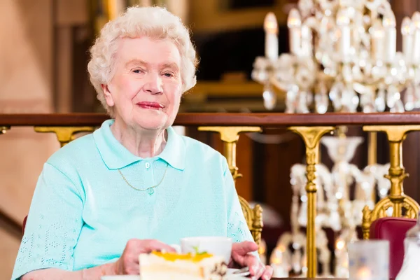 Старшая женщина с кофе и тортом в кафе — стоковое фото