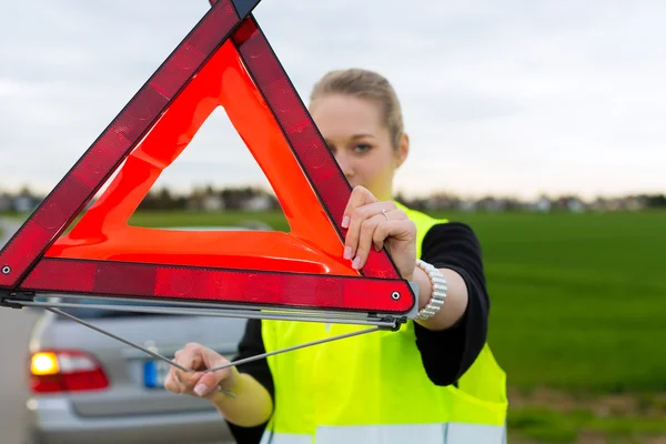 Young woman with warning triangle on street — Stock Photo, Image