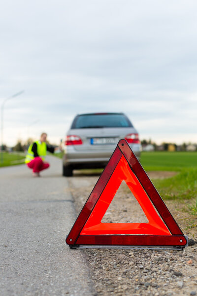 Young woman with warning triangle on street