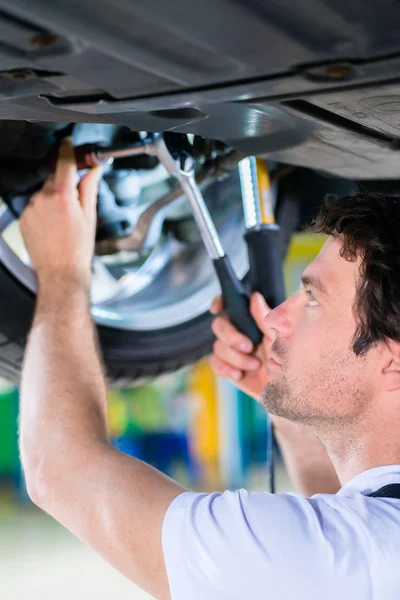 Mechanic working in car workshop on wheel — Stock Photo, Image
