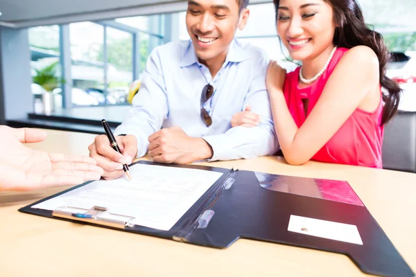 Pareja firma contrato de venta de coche en la concesionaria — Foto de Stock