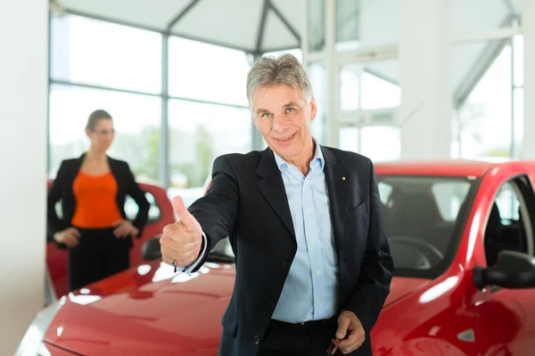 Man with woman and auto in car dealership — Stock Photo, Image