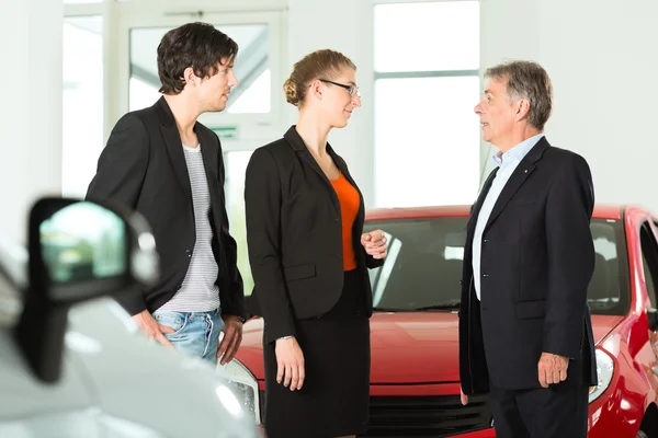 Man with couple and autos in car dealership — Stock Photo, Image