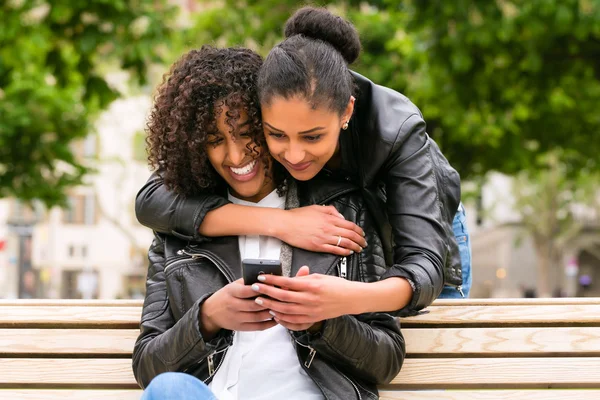 Friends chatting with smartphone on park bench — Stock Photo, Image