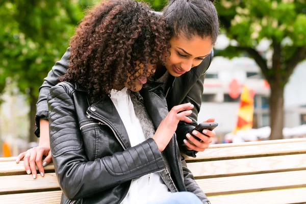 Друзі спілкуються зі смартфоном на лавці парку — стокове фото