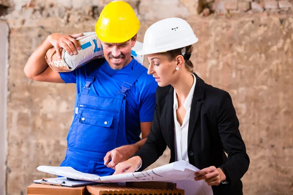 Architect and construction worker on site with plan — Stockfoto