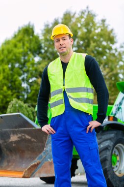 Builder on site in front of construction machinery
