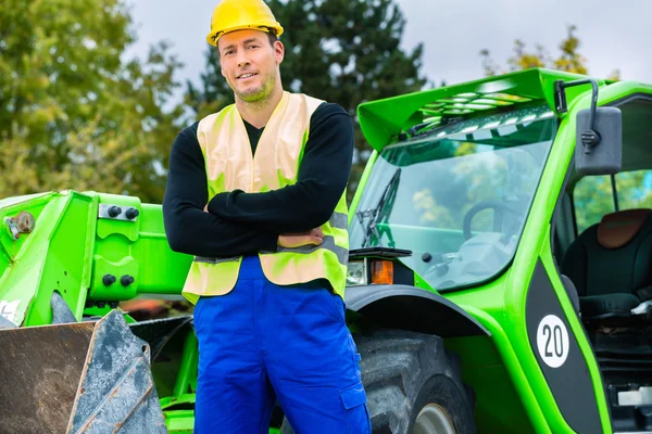 Builder in front of construction machinery — Stock Photo, Image