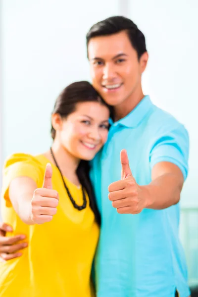 Jovem casal asiático no apartamento com polegares para cima — Fotografia de Stock