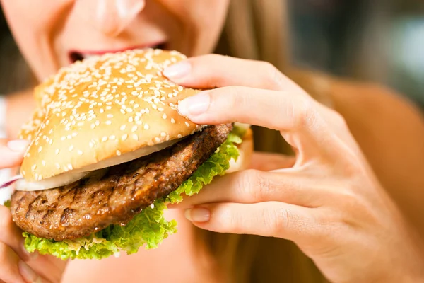 Mulher em um restaurante comer hambúrguer — Fotografia de Stock