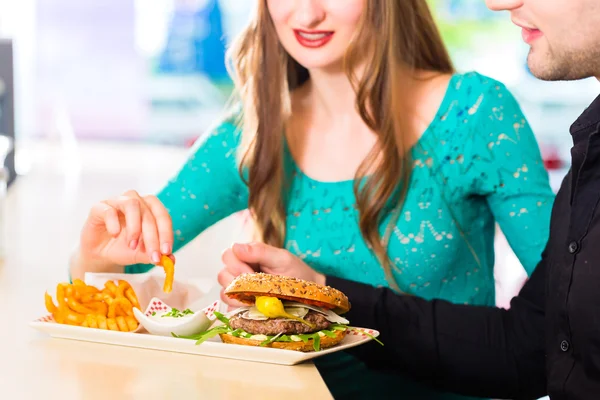 Pareja comiendo comida rápida con hamburguesas y papas fritas —  Fotos de Stock