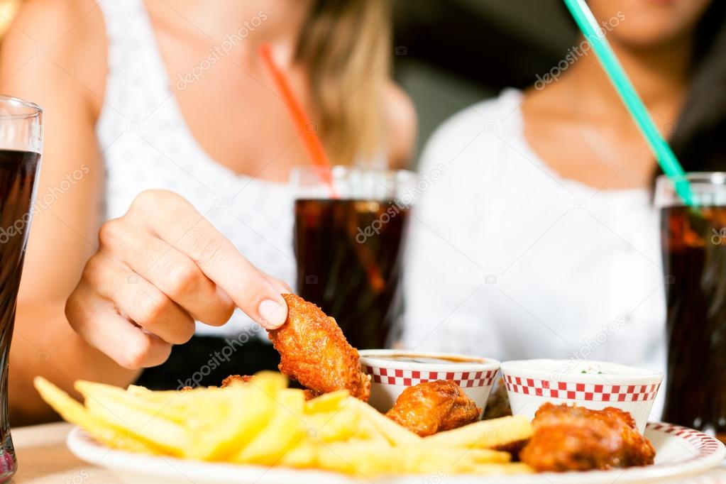 women eating chicken wings and drinking soda