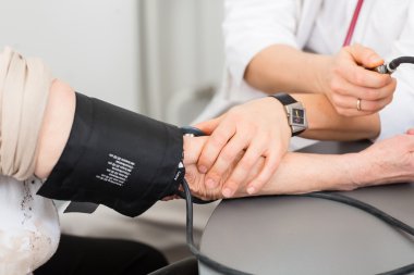 Doktor yaşlı bir hastanın tansiyonunu ölçüyor.