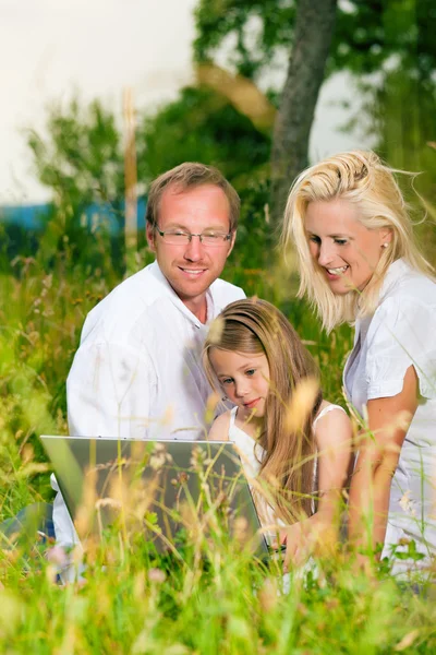 Lycklig familj sitter i äng med bärbar dator — Stockfoto